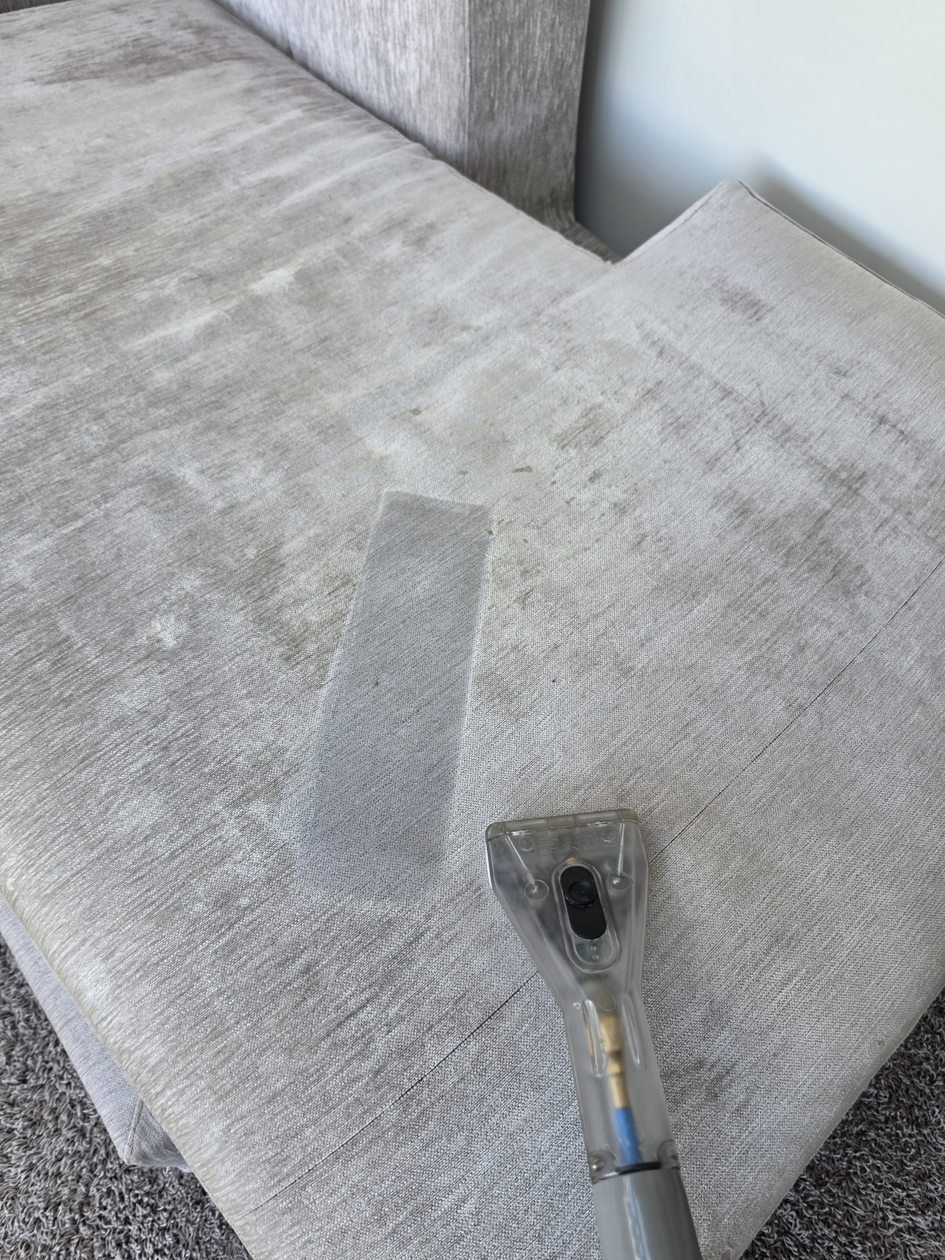 Upholstery extraction tool cleaning a light fabric sofa cushion