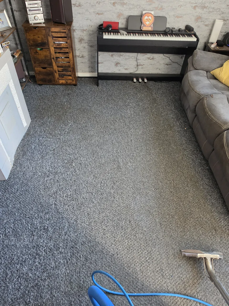 Do You Need to Move Furniture Before Carpet Cleaning? 1 Carpet cleaning wand on grey carpet beside a sofa, wooden cabinet and digital piano