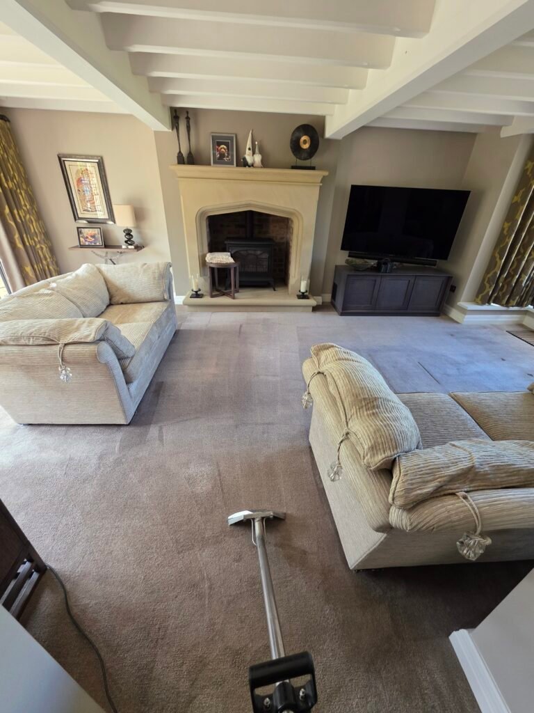 Carpet cleaning in a living room with cream sofas and a fireplace